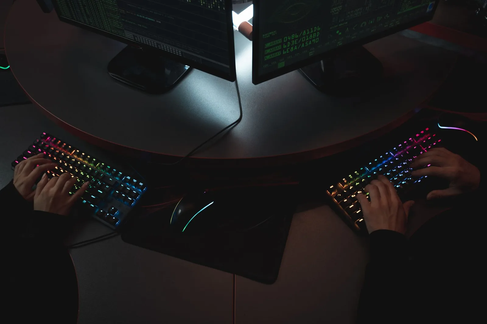 Kädet kirjoittavat RGB-näppäimistöillä pimeässä pelihuoneessa
