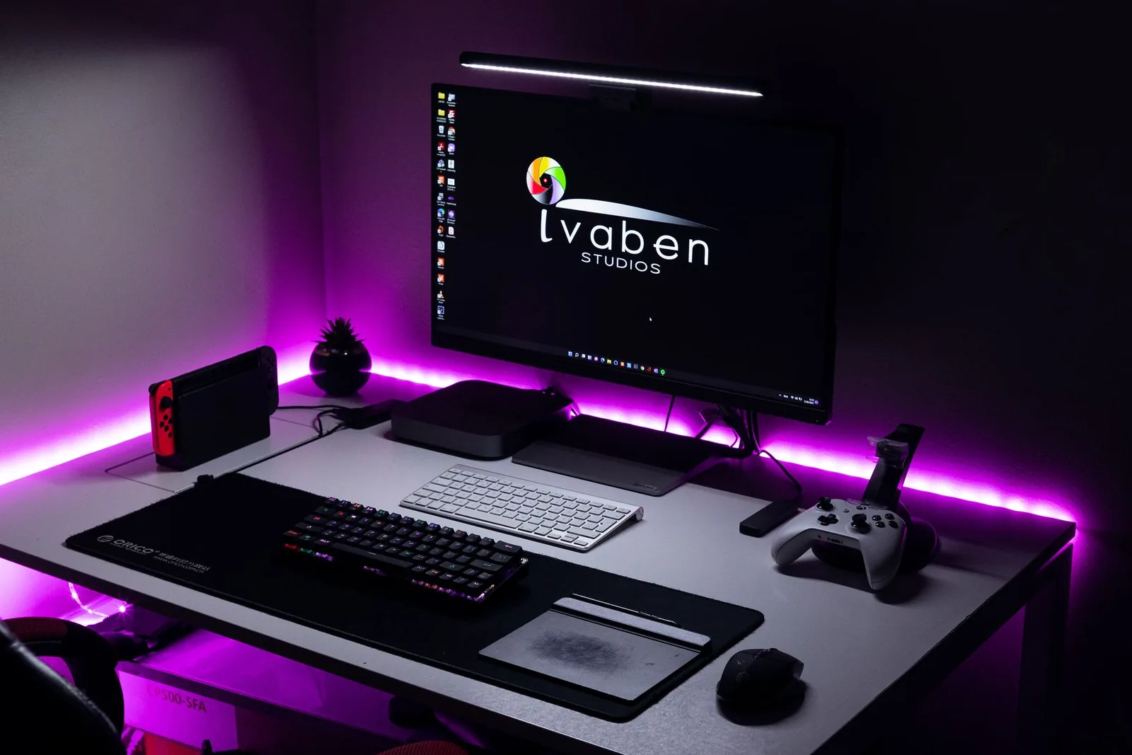 Violetein LED-valoin valaistu pelipöytä ja tietokone